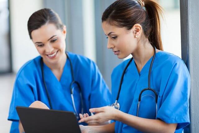 Nurses Collaborate over a laptop monitor regarding a patient's health information.